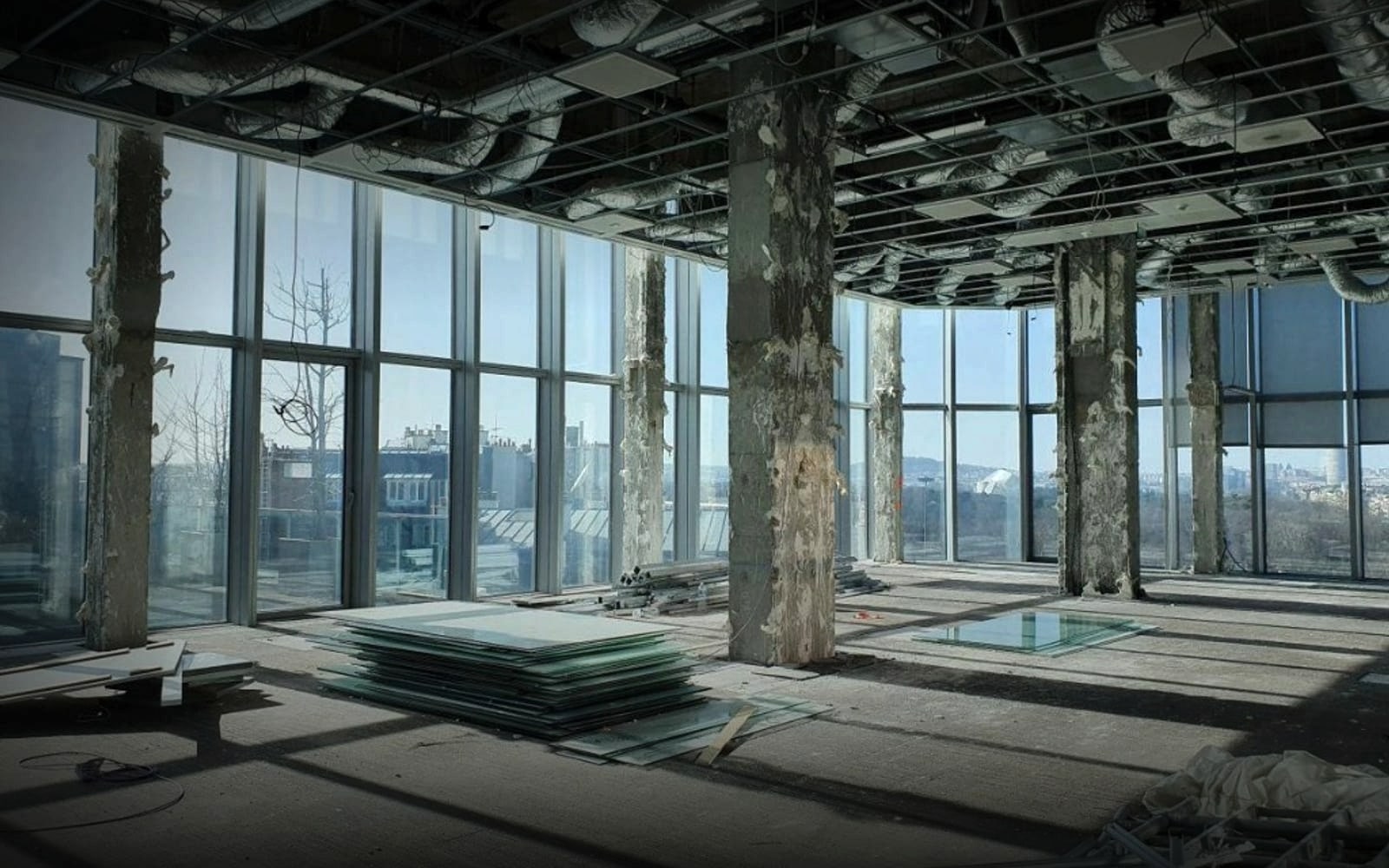 Chantier de déconstruction d'un immeuble de bureaux à Paris - colonnes en béton dénudées, vitrages empilés au sol prêts au réemploi et grandes baies vitrées ouvrant sur la ville