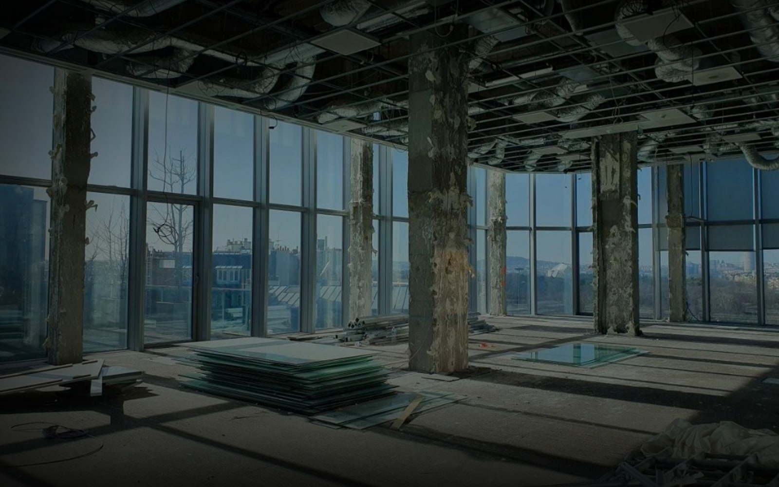 Chantier de déconstruction d'un immeuble de bureaux à Paris - colonnes en béton dénudées, vitrages empilés au sol prêts au réemploi et grandes baies vitrées ouvrant sur la ville