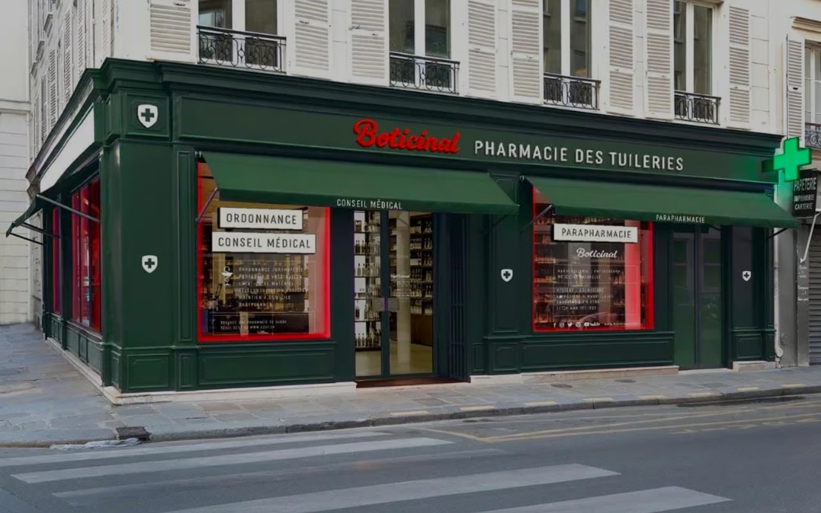 Devanture d'une pharmacie Boticinal éclairée, avec enseigne rouge néon