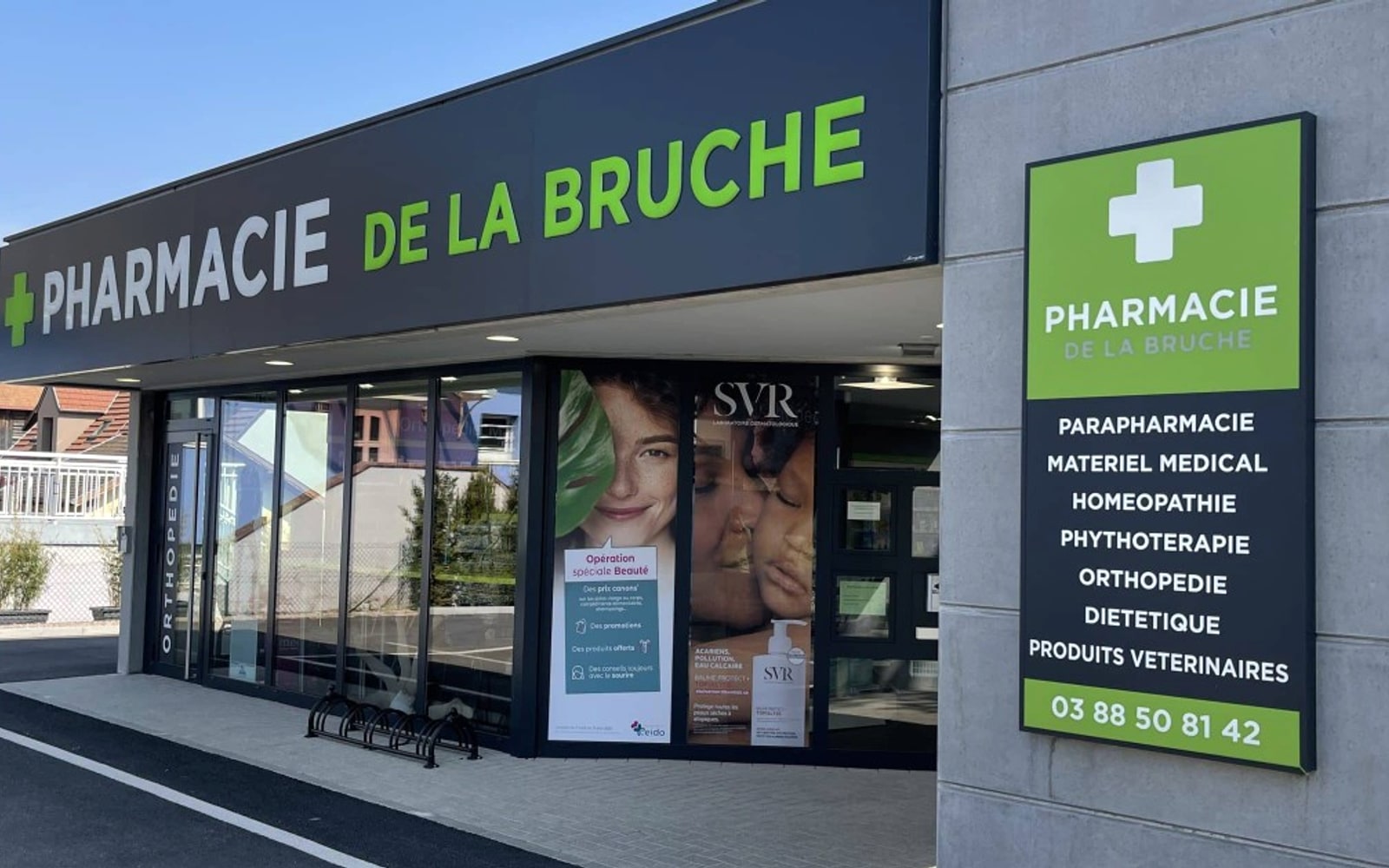 Devanture de la Pharmacie de la Bruche, officine adhérente du groupement CEIDO - enseigne navy et verte, totem croix pharmacie et baies vitrées