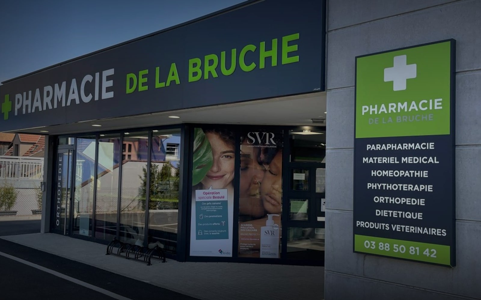 Devanture de la Pharmacie de la Bruche, officine adhérente du groupement CEIDO - enseigne navy et verte, totem croix pharmacie et baies vitrées