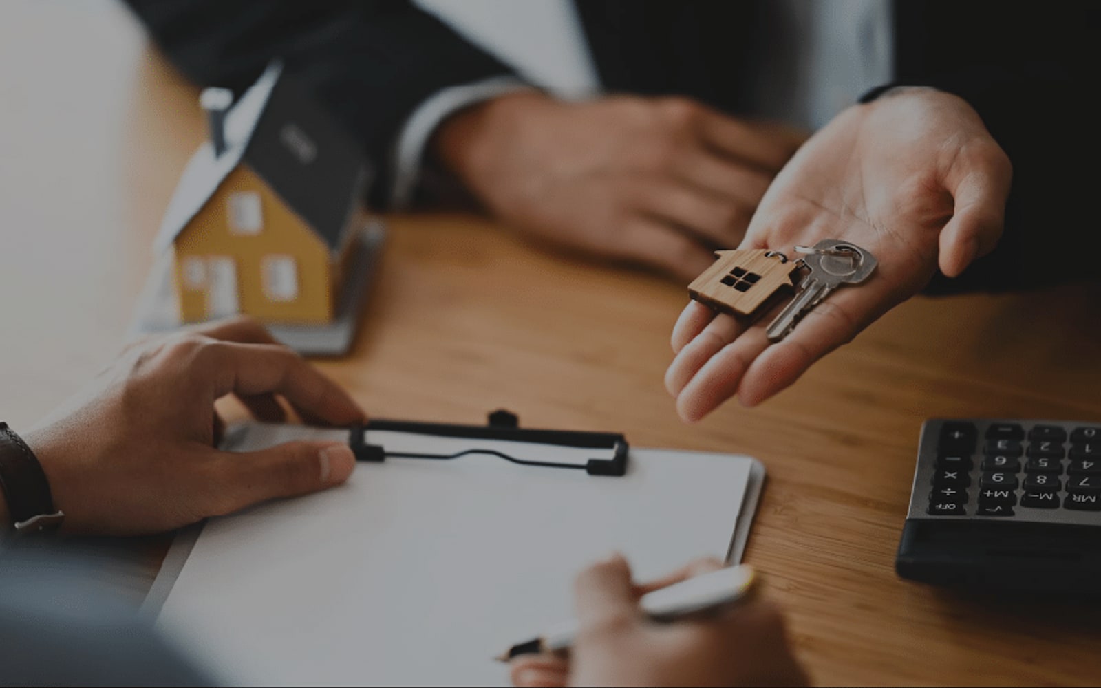 Remise des clés d'un bien immobilier - porte-clés en bois en forme de maison, presse-papier et calculatrice sur un bureau